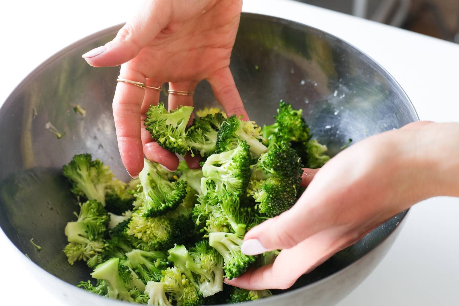 Tossing broccoli in a bowl with olive oil.