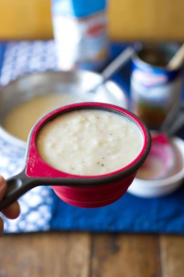 This is a super easy recipe for making your own homemade cream of chicken soup. Just four ingredients and sooo delicious! | pinchofyum.com White hand holding a measuring cup filled with cream of chicken soup.
