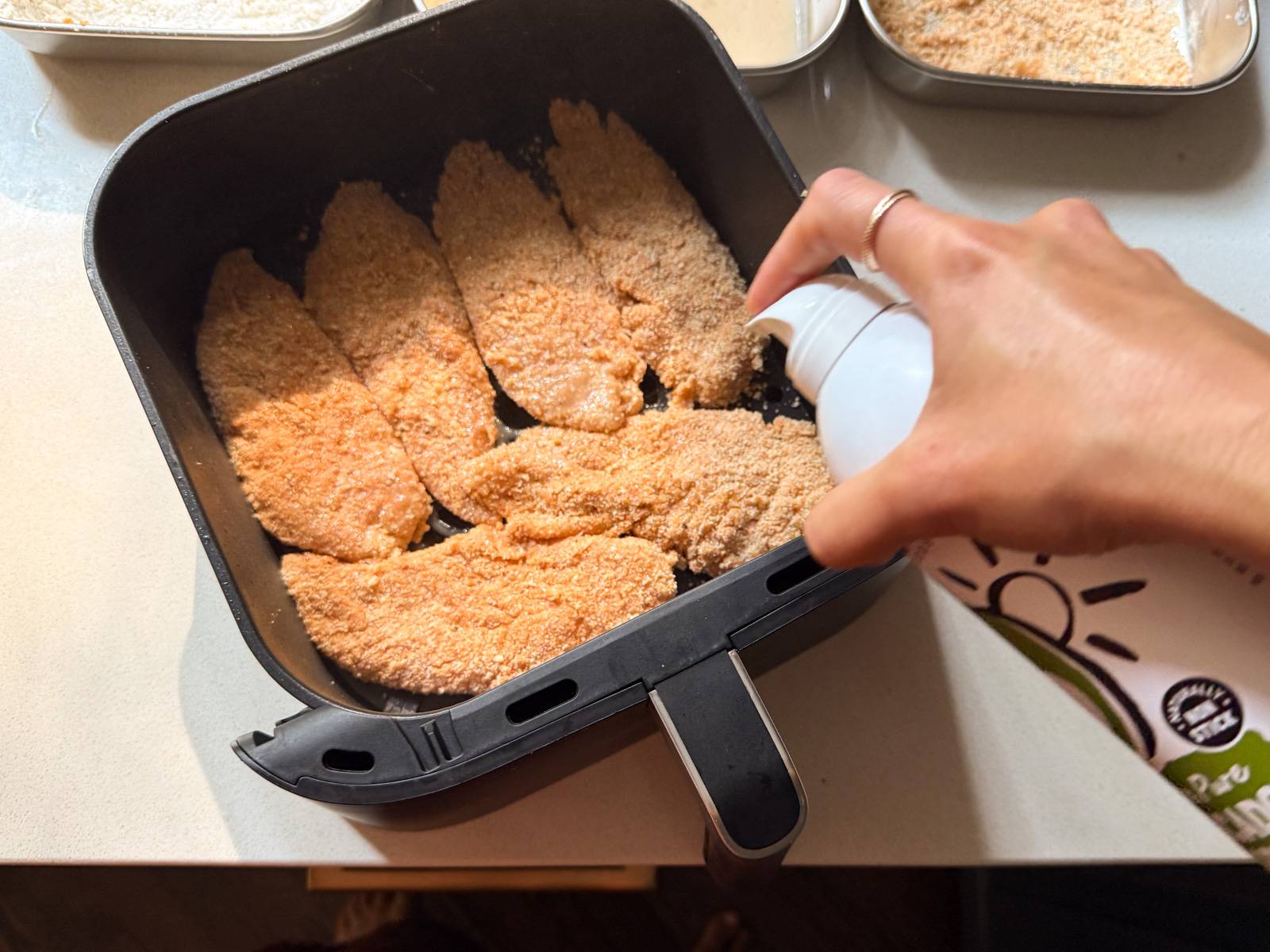 Spraying chicken tenderloins with avocado spray.