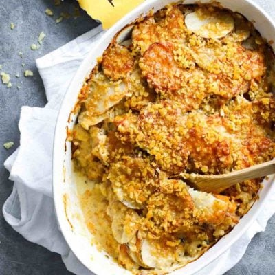 Garlic Herb Cheesy Potatoes in a casserole dish with a spoon.